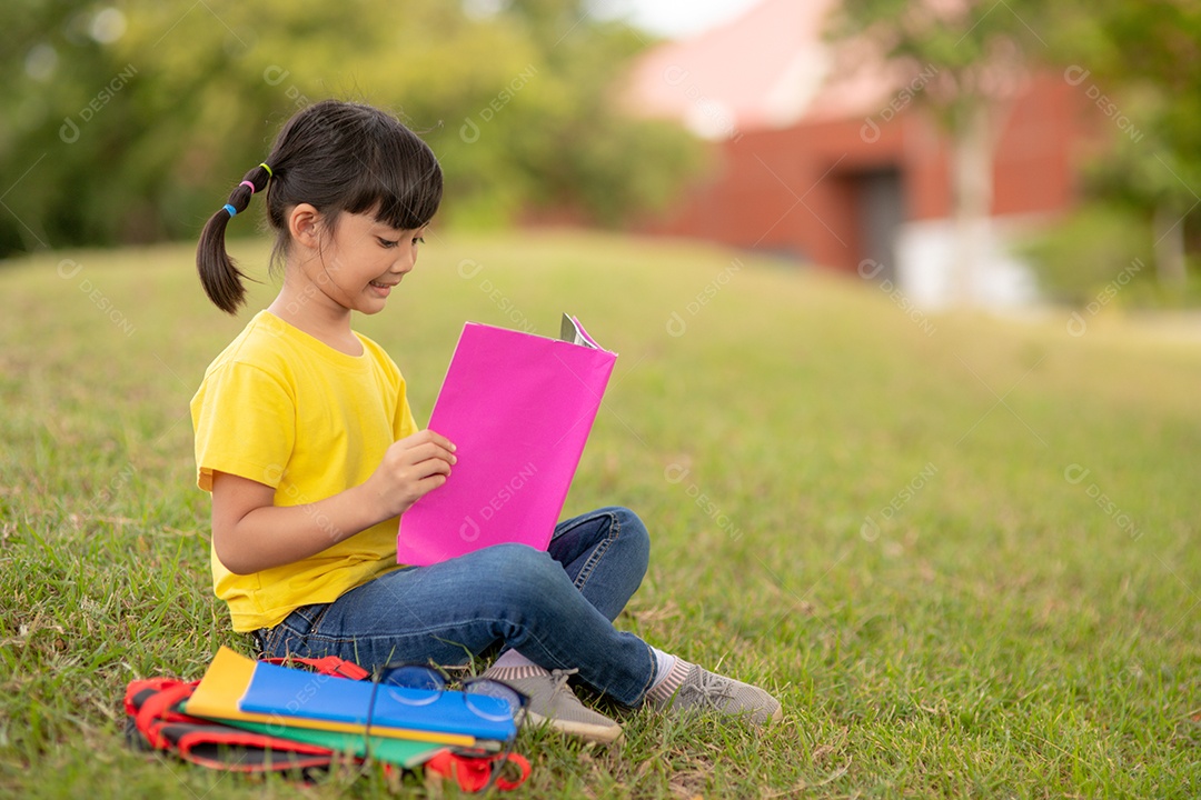 Menina bonitinha lendo livro sentado sobre gramado verde parque