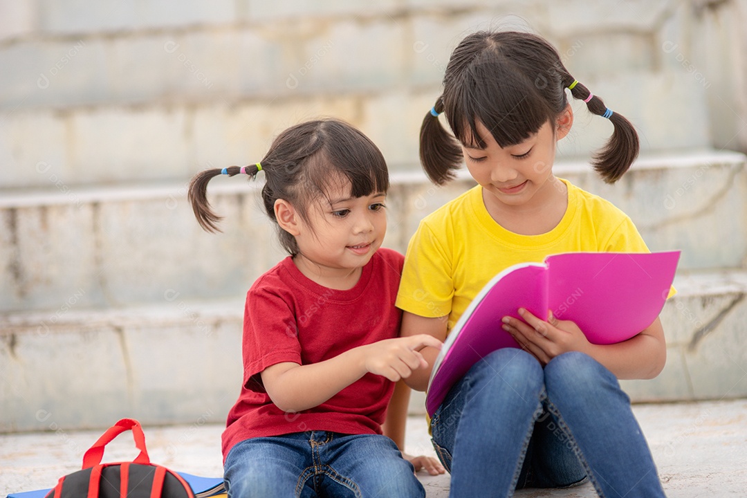 Menina e irmã lendo um livro juntos. Adorável asiático