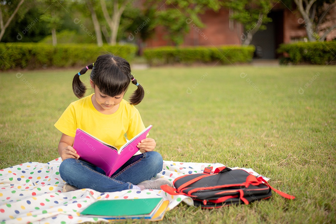 Menina bonitinha lendo livro fora na grama