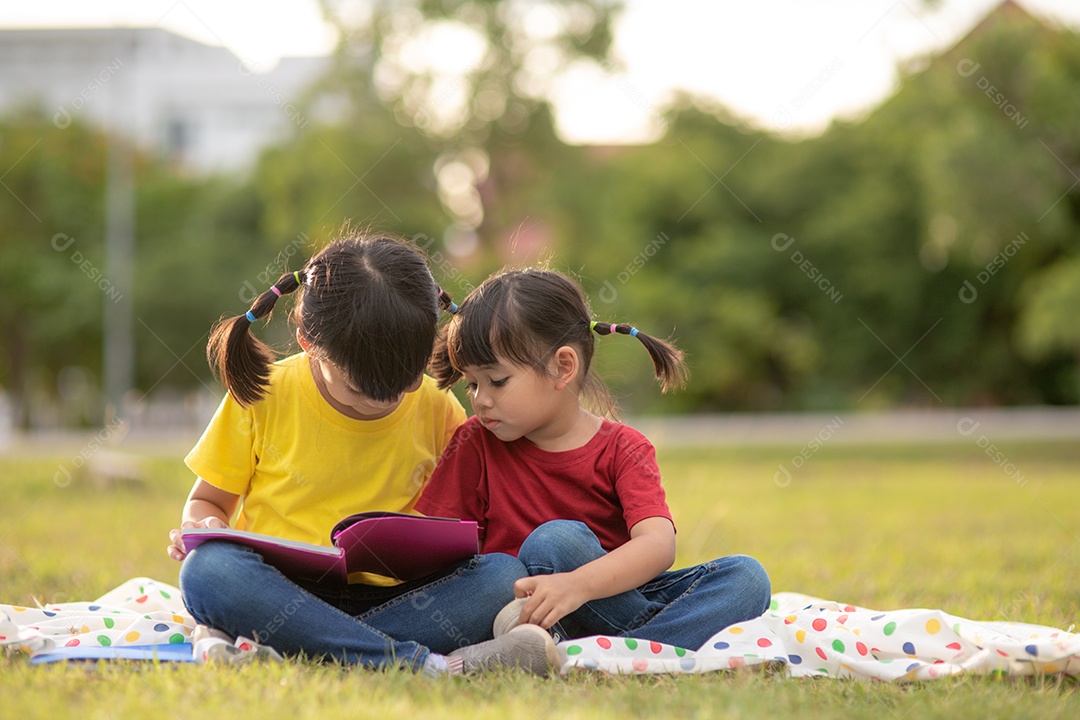 Two beautiful little girls reading books in the garden, sitting.