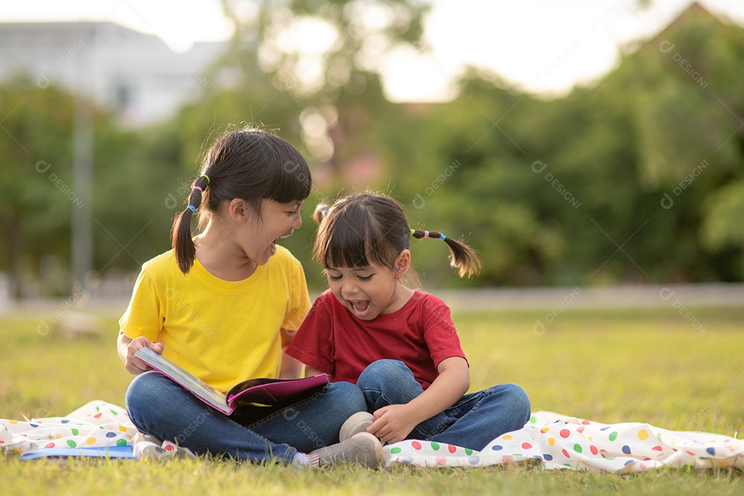 Duas lindas garotinhas lendo livros no jardim, sentadas.