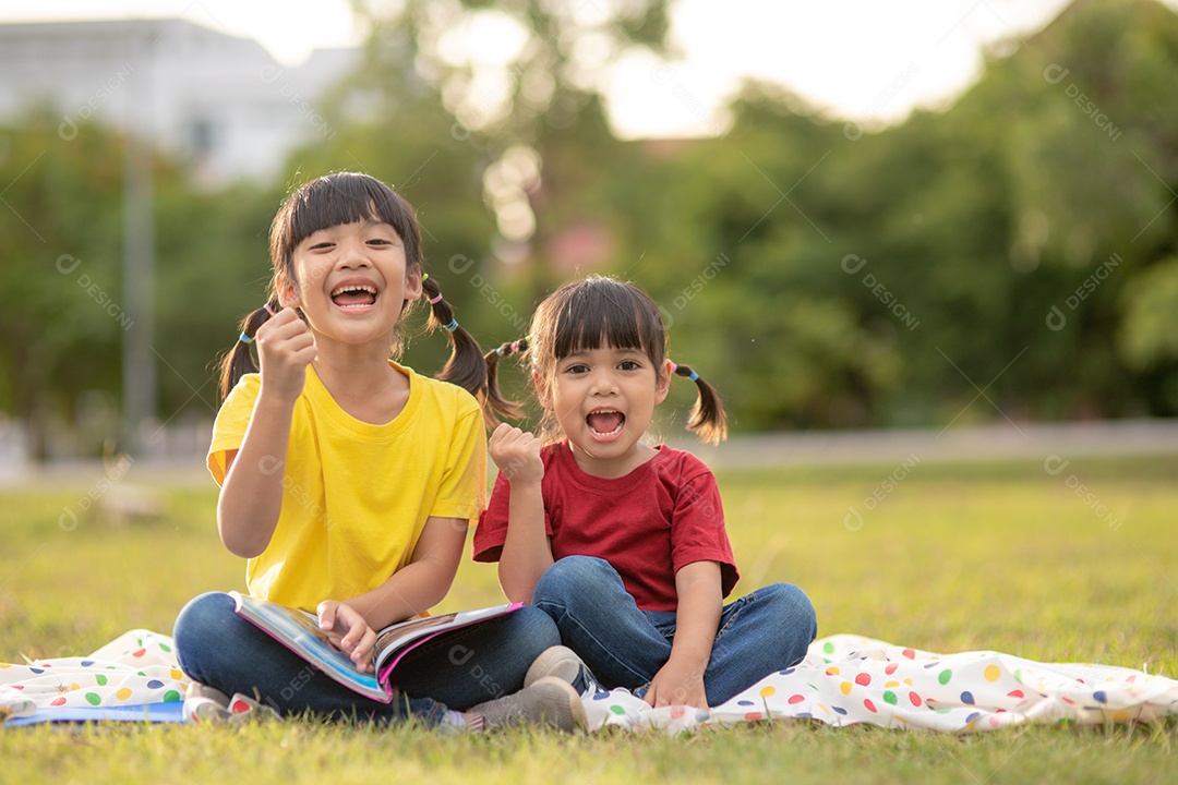 Duas lindas garotinhas lendo livros no jardim, sentadas.