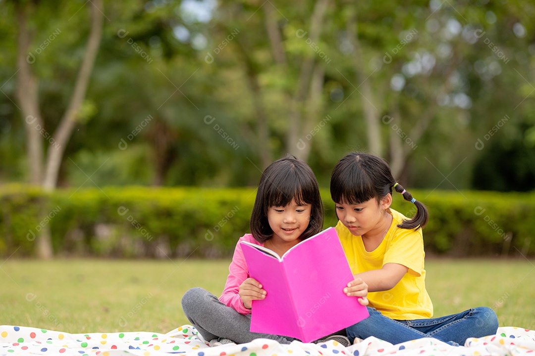 Duas lindas garotinhas lendo livros no jardim, sentadas.