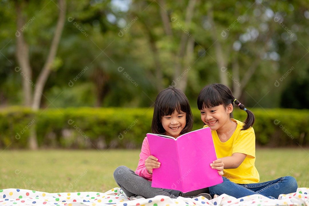 Duas lindas garotinhas lendo livros no jardim, sentadas.