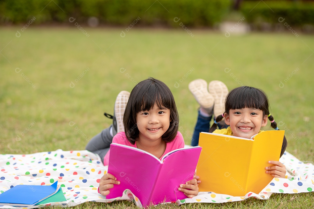 Duas lindas garotinhas lendo livros no jardim, sentadas.