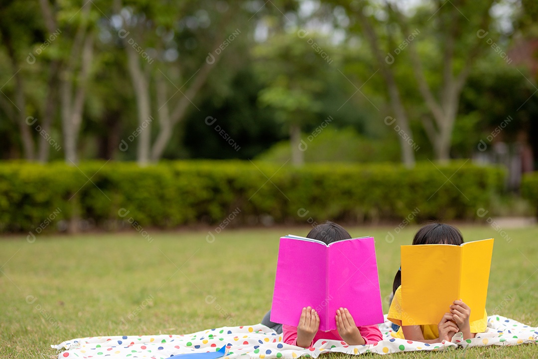 Duas lindas garotinhas lendo livros no jardim, sentadas.