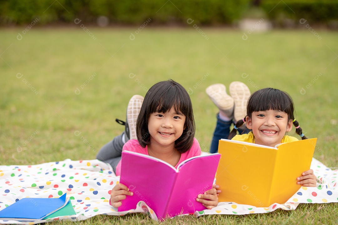 Duas lindas garotinhas lendo livros no jardim, sentadas.