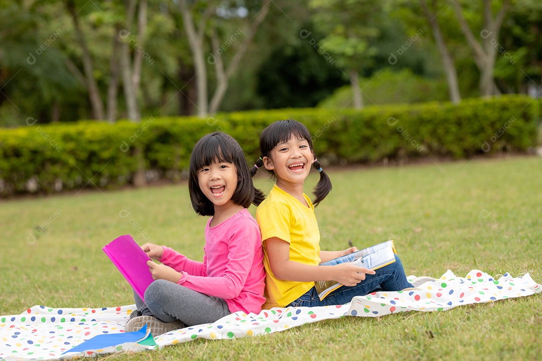 Duas lindas garotinhas lendo livros no jardim, sentadas.