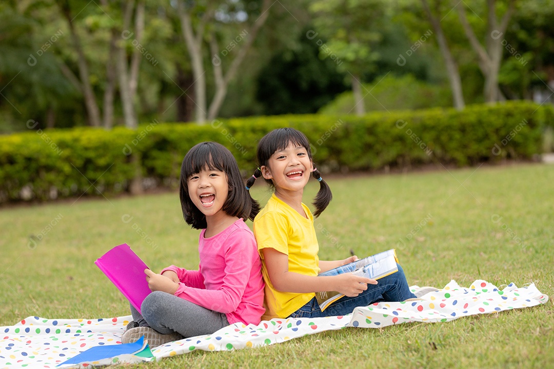 Duas lindas garotinhas lendo livros no jardim, sentadas.