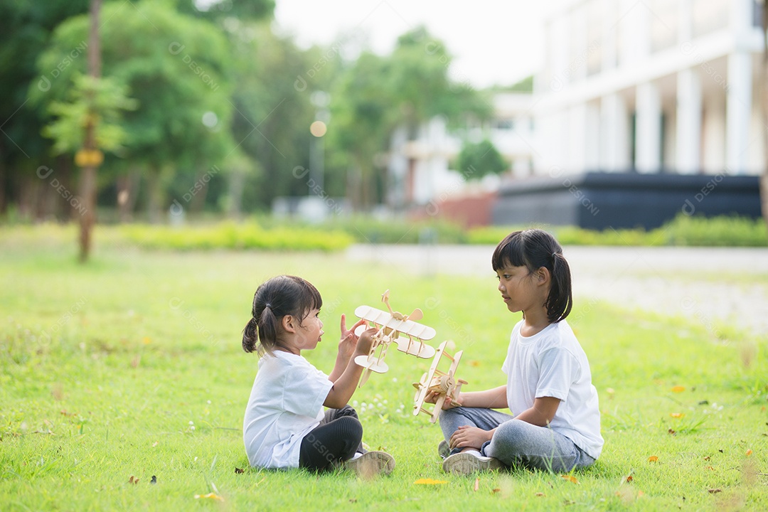 Duas crianças brincando com avião de brinquedo de papelão no parque