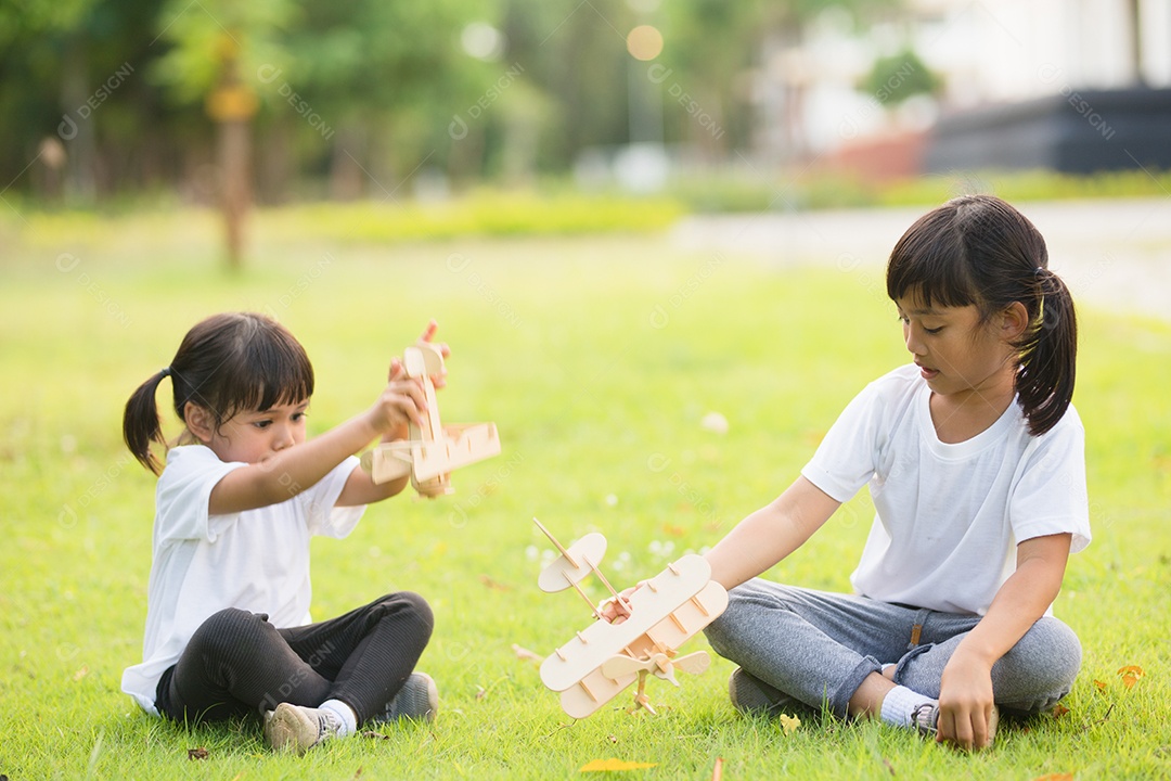 Duas crianças brincando com avião de brinquedo de papelão no parque