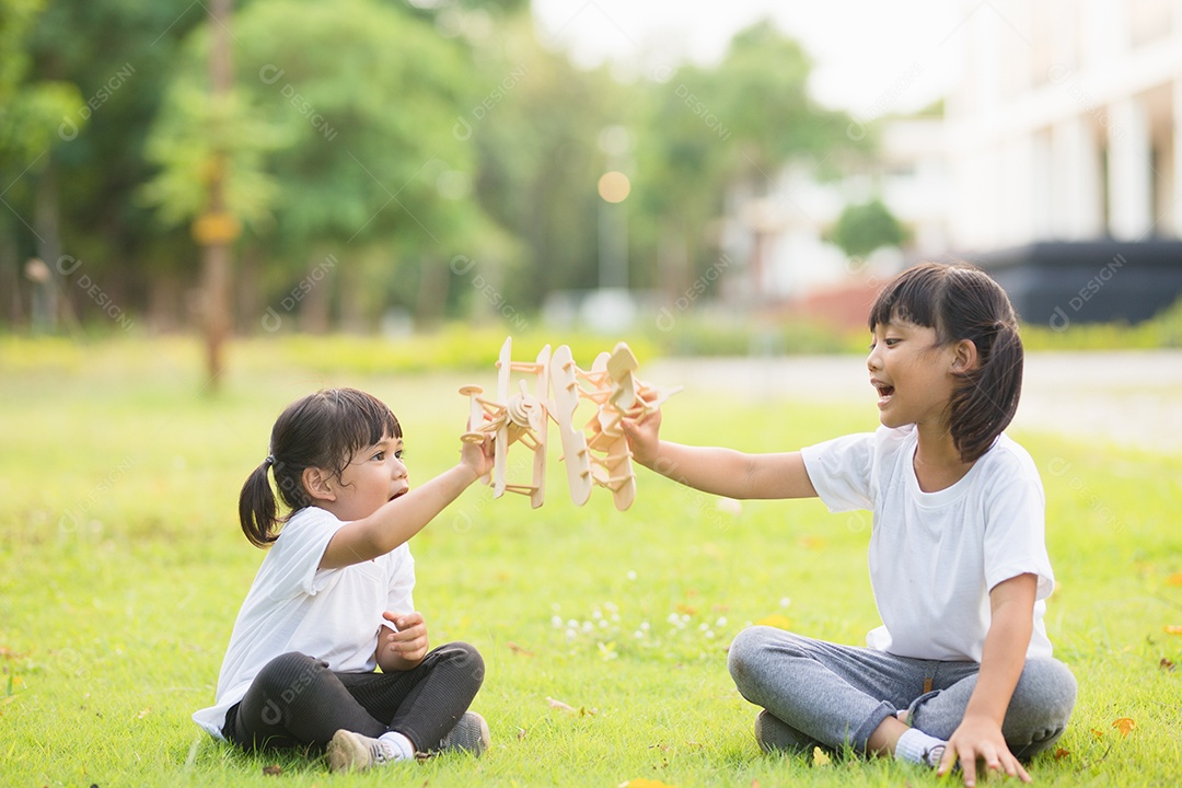 Duas crianças brincando com avião de brinquedo de papelão no parque