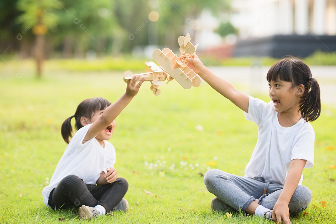 Duas crianças brincando com avião de brinquedo de papelão no parque