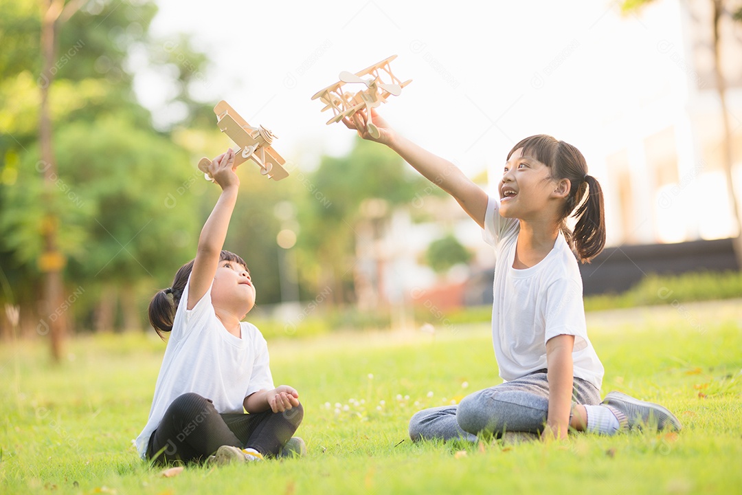 Duas crianças brincando com avião de brinquedo de papelão no parque
