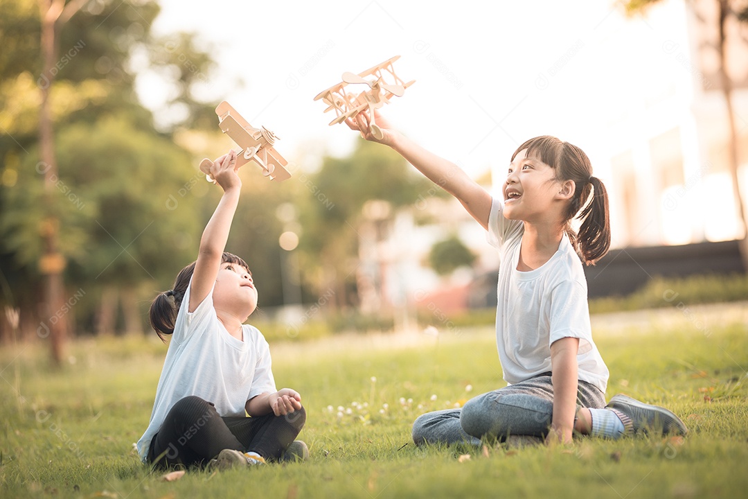 Duas crianças brincando com avião de brinquedo de papelão no parque