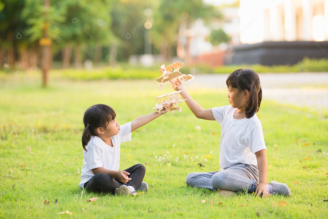 Duas crianças brincando com avião de brinquedo de papelão no parque