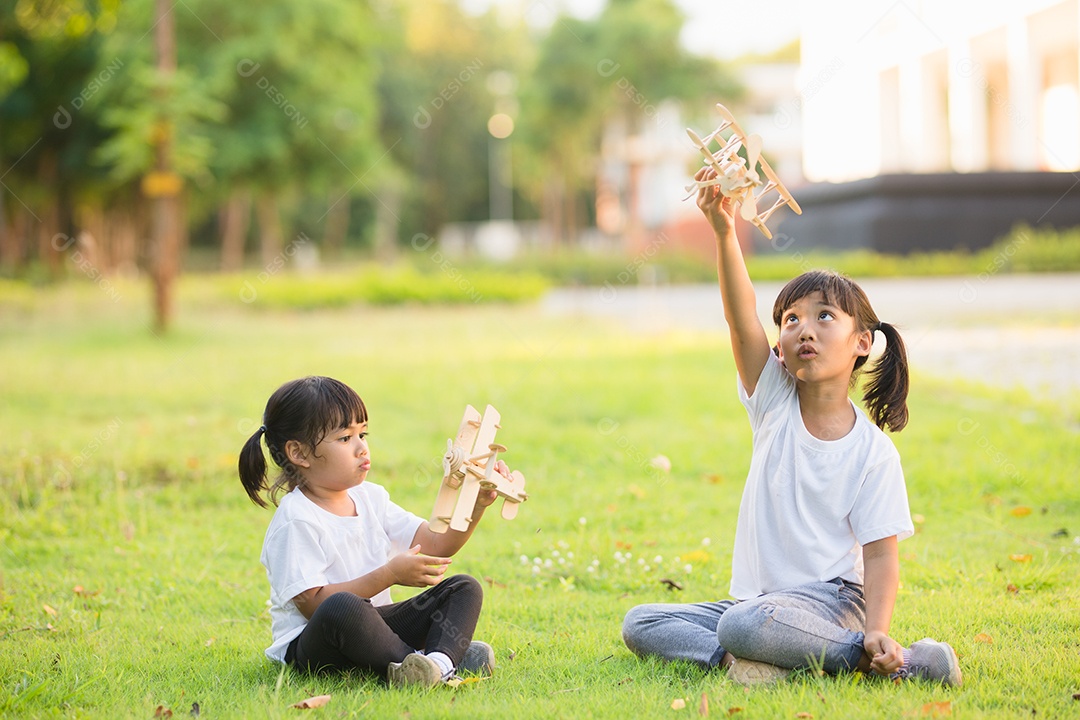 Duas crianças brincando com avião de brinquedo de papelão no parque