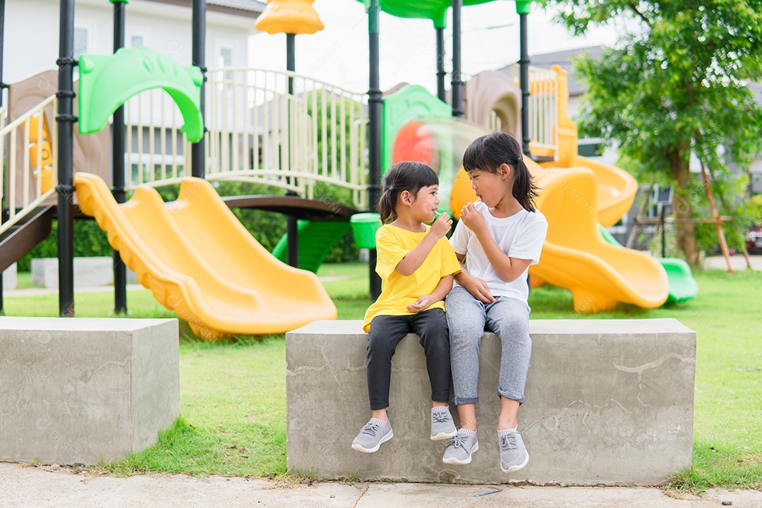 Duas crianças brincam e comem pirulitos no Parque infantil