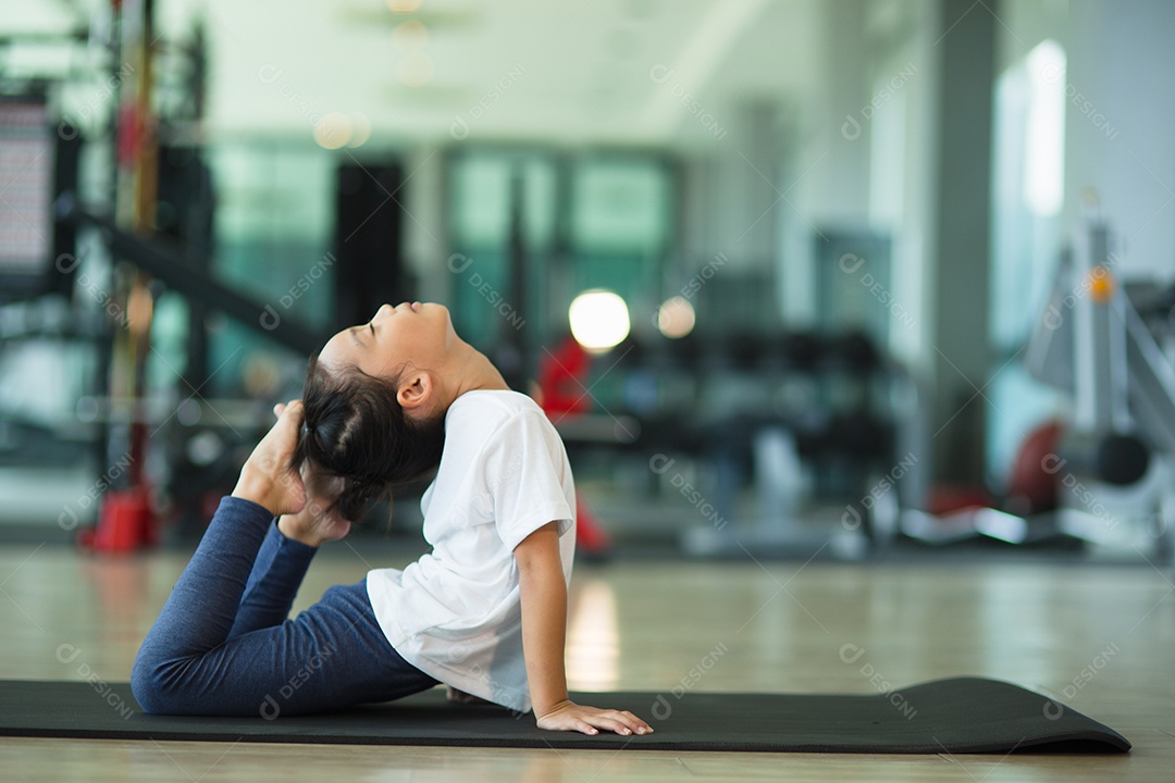 Menina bonitinha praticando pose de ioga em um tapete interior