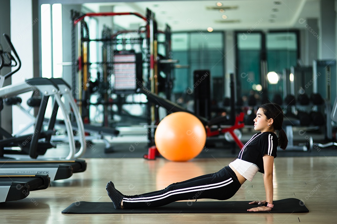 Menina bonitinha praticando pose de ioga em um tapete interior