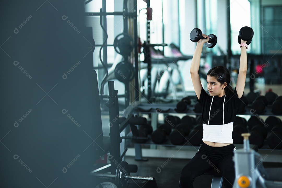 Linda jovem fazendo exercícios com halteres no ginásio.