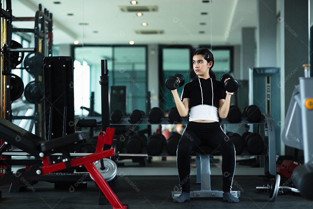 Linda jovem fazendo exercícios com halteres no ginásio.