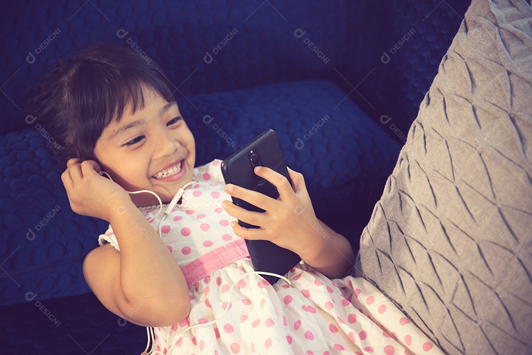 Linda garotinha em fones de ouvido usando smartphone em um sofá