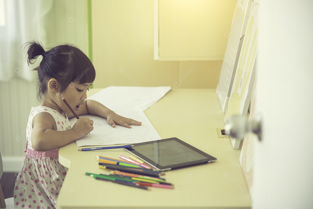 Criança asiática usando um lápis para escrever no caderno na mesa