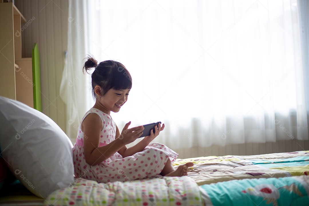 Criança asiática usando fone de ouvido para ouvir música pelo smartphone