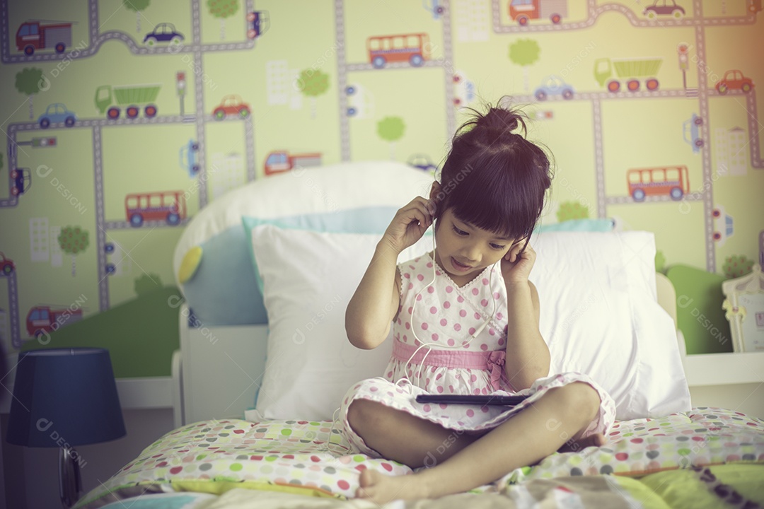 Criança asiática usando fone de ouvido para ouvir música pelo smartphone