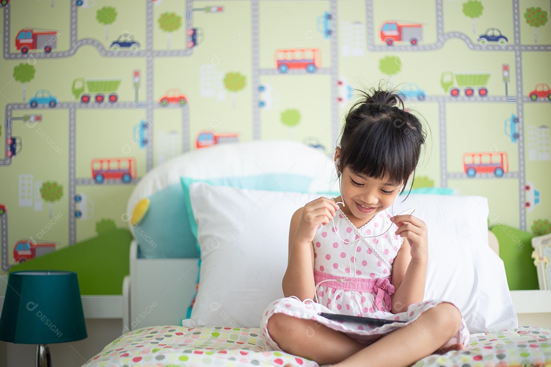 Criança asiática usando fone de ouvido para ouvir música pelo smartphone