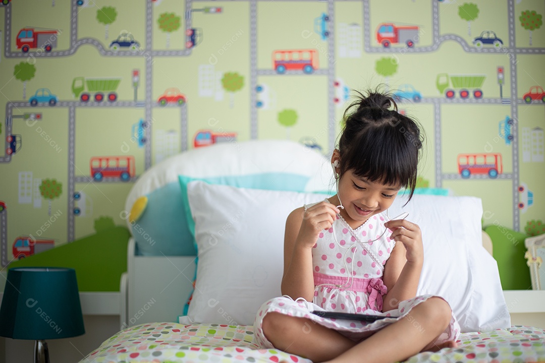 Criança asiática usando fone de ouvido para ouvir música pelo smartphone