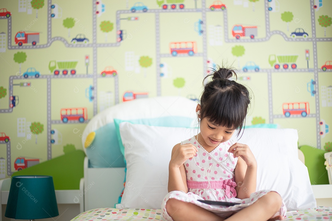 Criança asiática usando fone de ouvido para ouvir música pelo smartphone