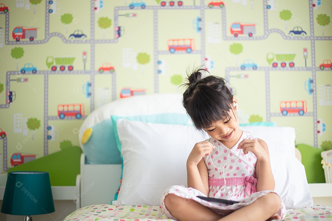 Criança asiática usando fone de ouvido para ouvir música pelo smartphone