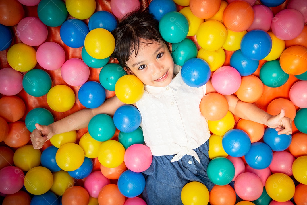 Menina asiática feliz jogando na piscina de bolas coloridas