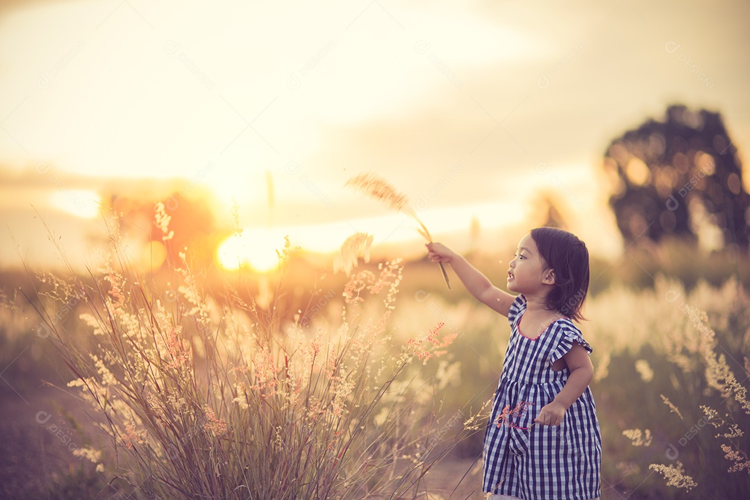 Garota bonita feliz em um campo jogando com picos naturais ao pôr do sol de verão