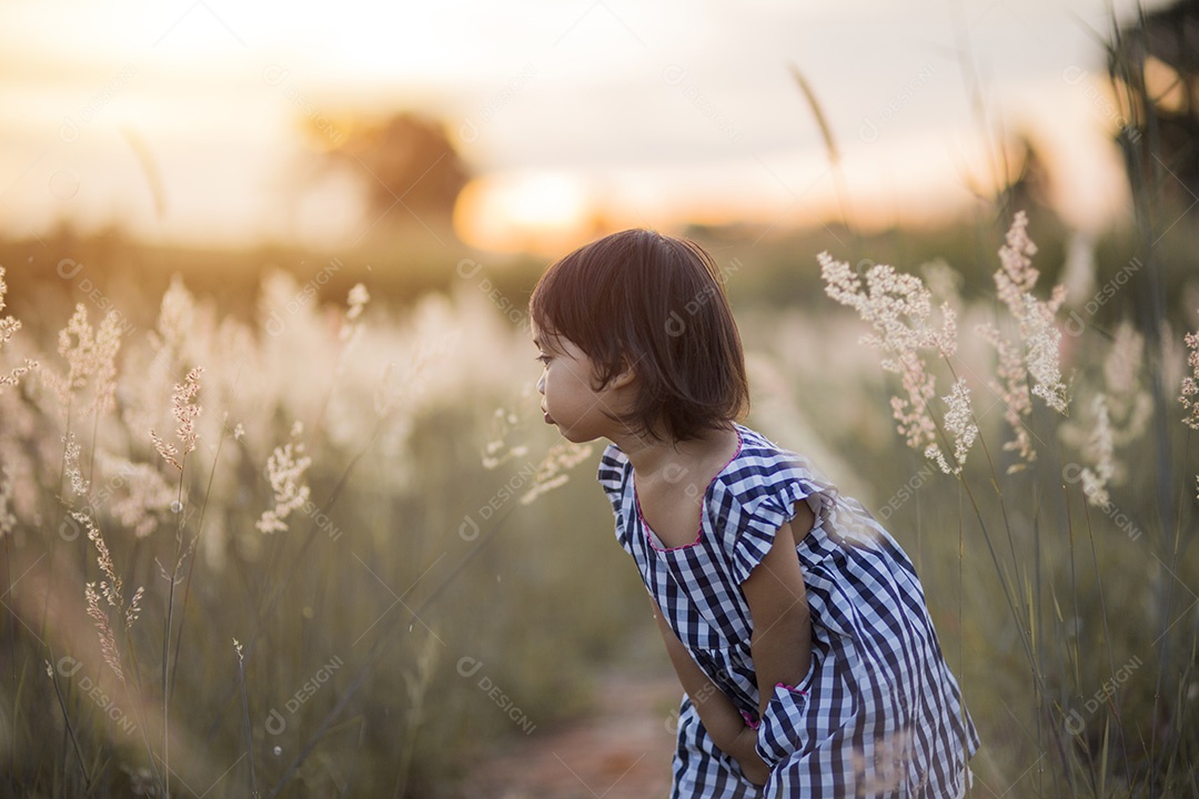 Garota bonita feliz em um campo jogando com picos naturais ao pôr do sol de verão