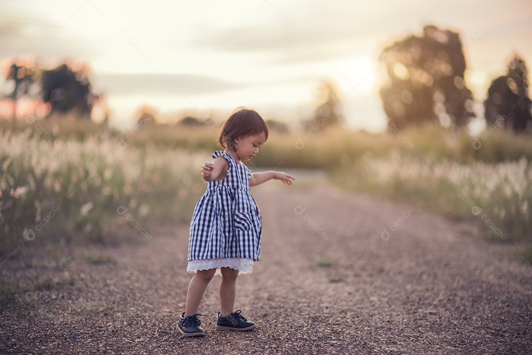 Garota bonita feliz em um campo jogando com picos naturais ao pôr do sol de verão