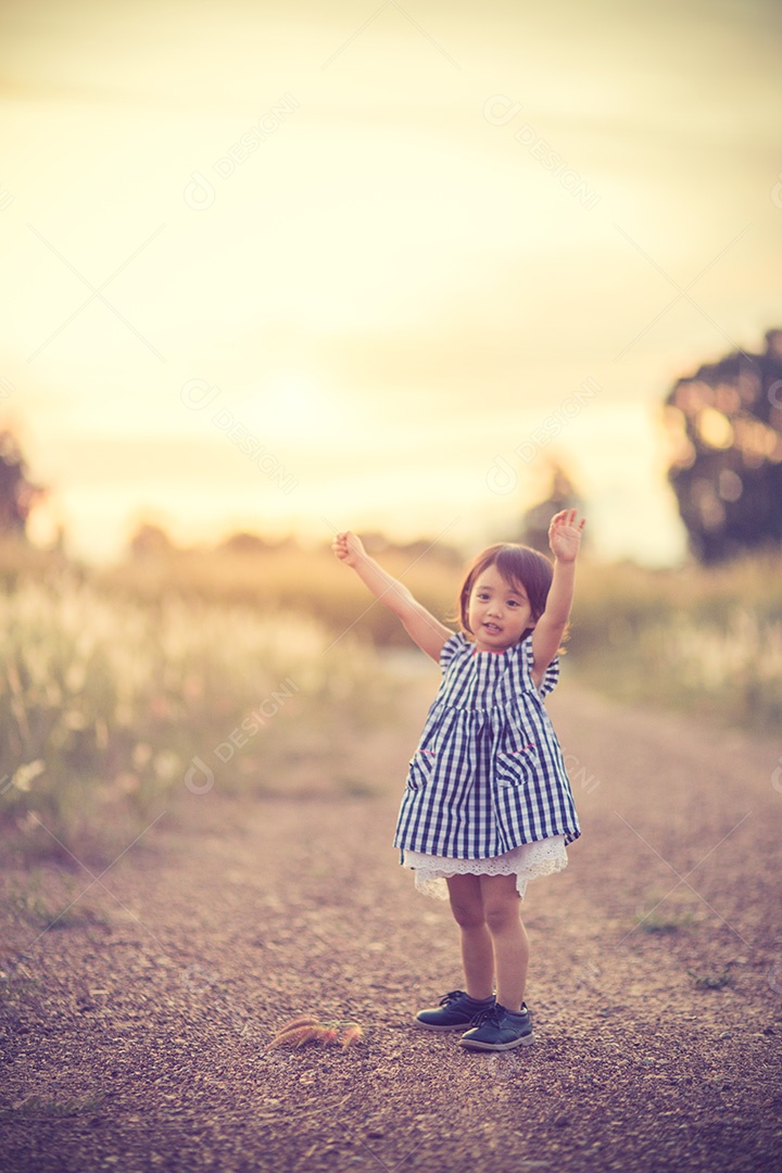 Garota bonita feliz em um campo jogando com picos naturais ao pôr do sol de verão.