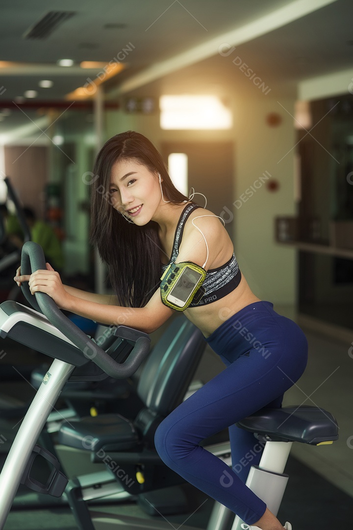 Mulher feliz andando de bicicleta ergométrica no ginásio