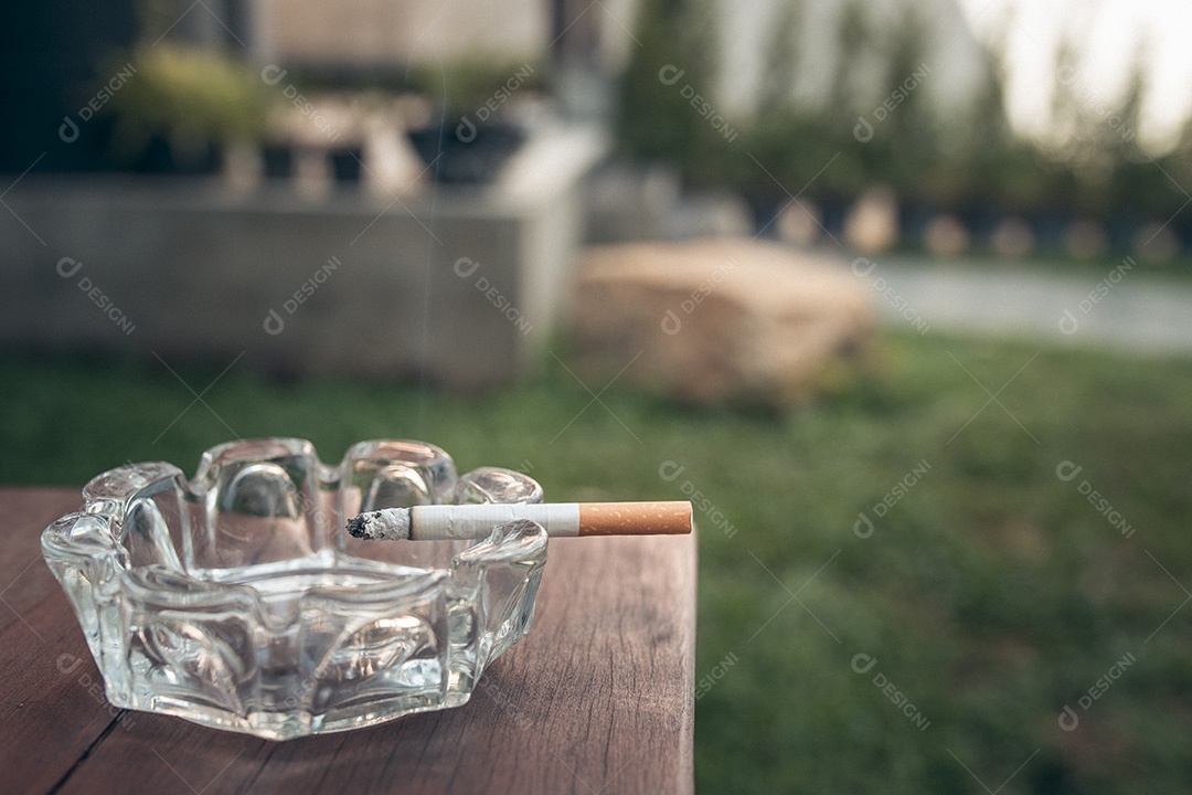 Aproximação do cigarro na borda do cinzeiro na mesa de madeira