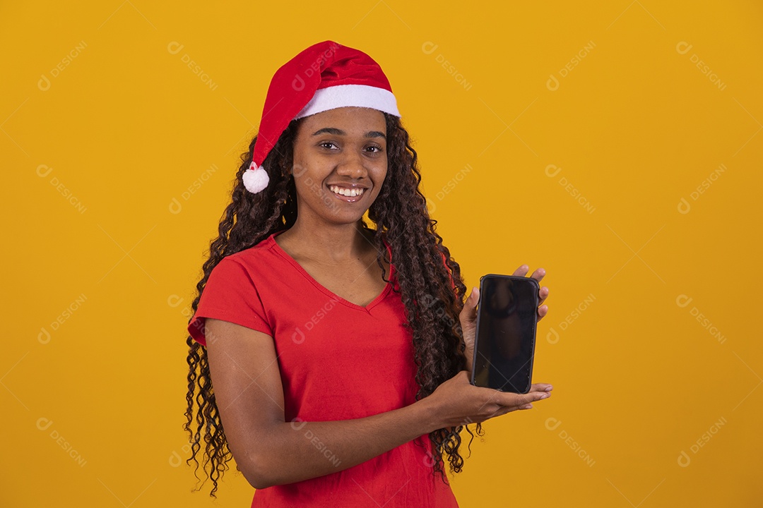 Linda mulher negra segurando celular usando gorro do papai noel Feliz Natal