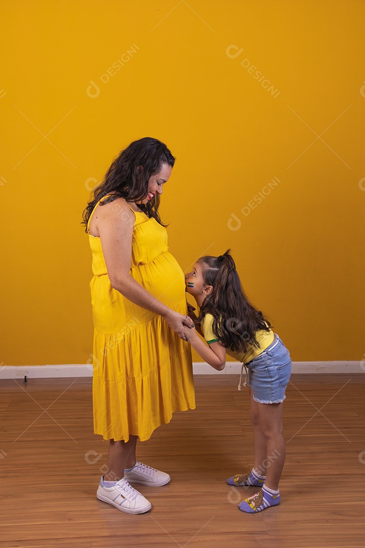 Mulher gestante usando vestido amarelo e criança fazendo caricias na barriga, temática copa do mundo