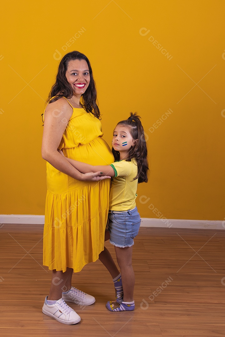 Mulher gestante usando vestido amarelo e criança fazendo caricias na barriga, temática copa do mundo