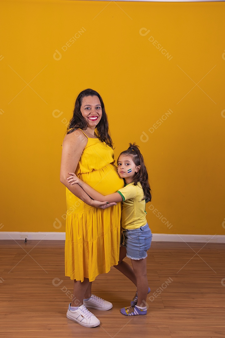 Mulher gestante usando vestido amarelo e criança fazendo caricias na barriga, temática copa do mundo