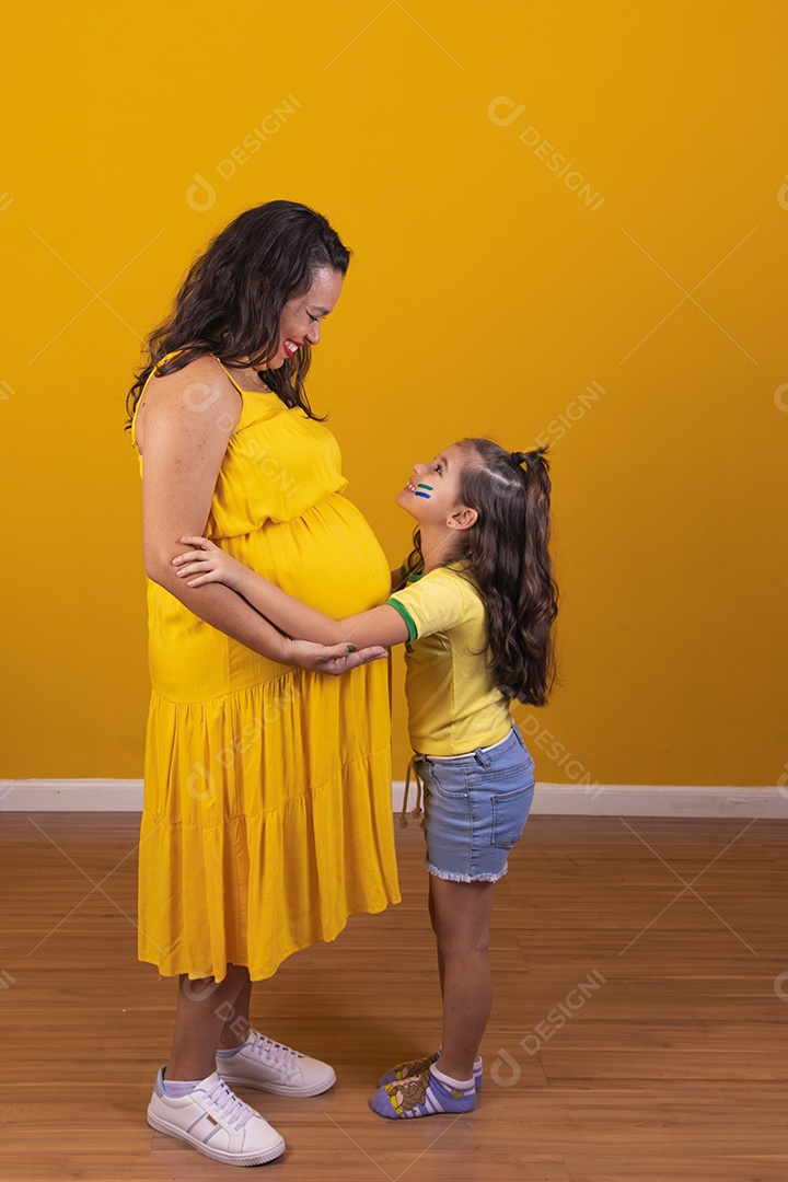 Mulher gestante usando vestido amarelo e criança fazendo caricias na barriga, temática copa do mundo