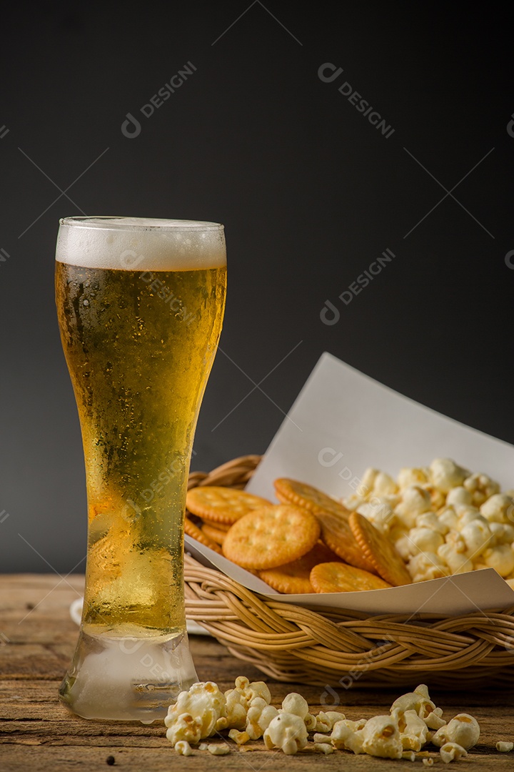 Copo de cerveja e pipoca em um fundo de madeira.