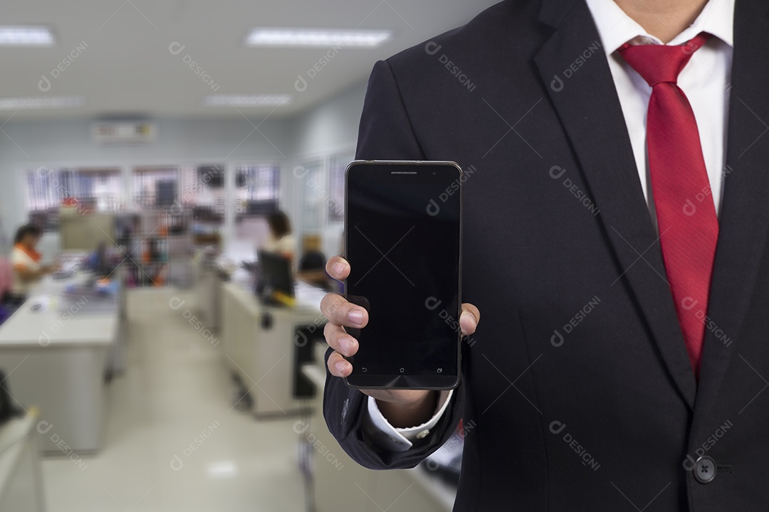 Homem de negócios que usa o telefone móvel esperto no fundo do escritório.