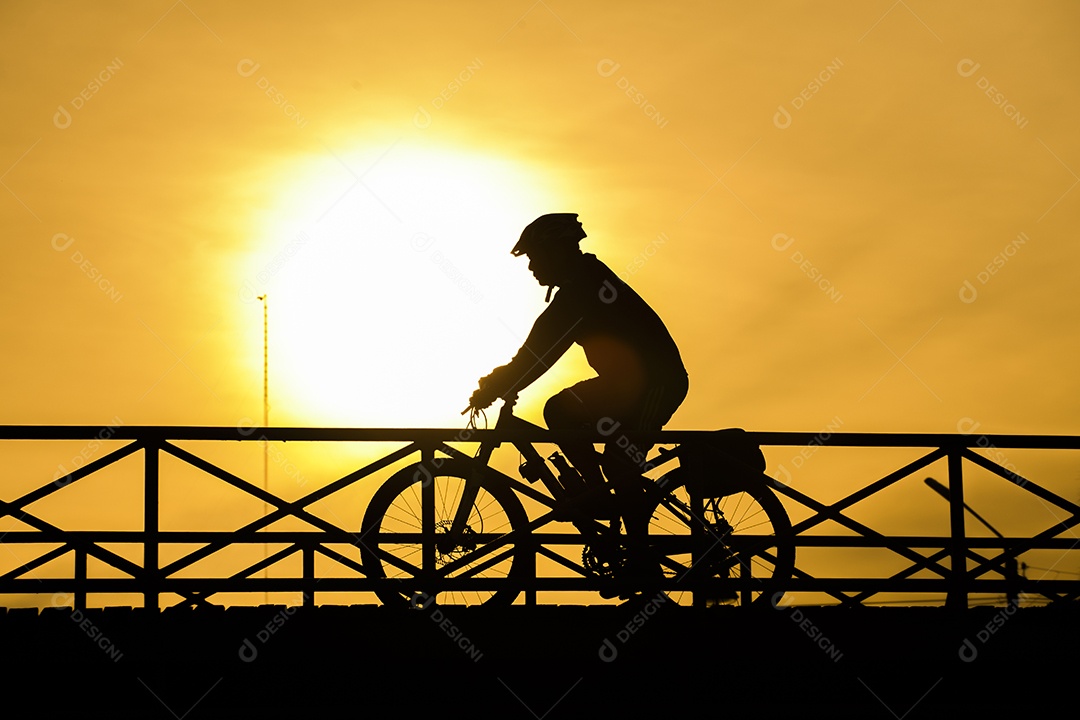 Silhueta de motociclista na ponte e pôr do sol.