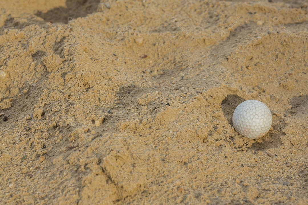 Bola de golfe iluminada pelo sol com sombra na armadilha de areia